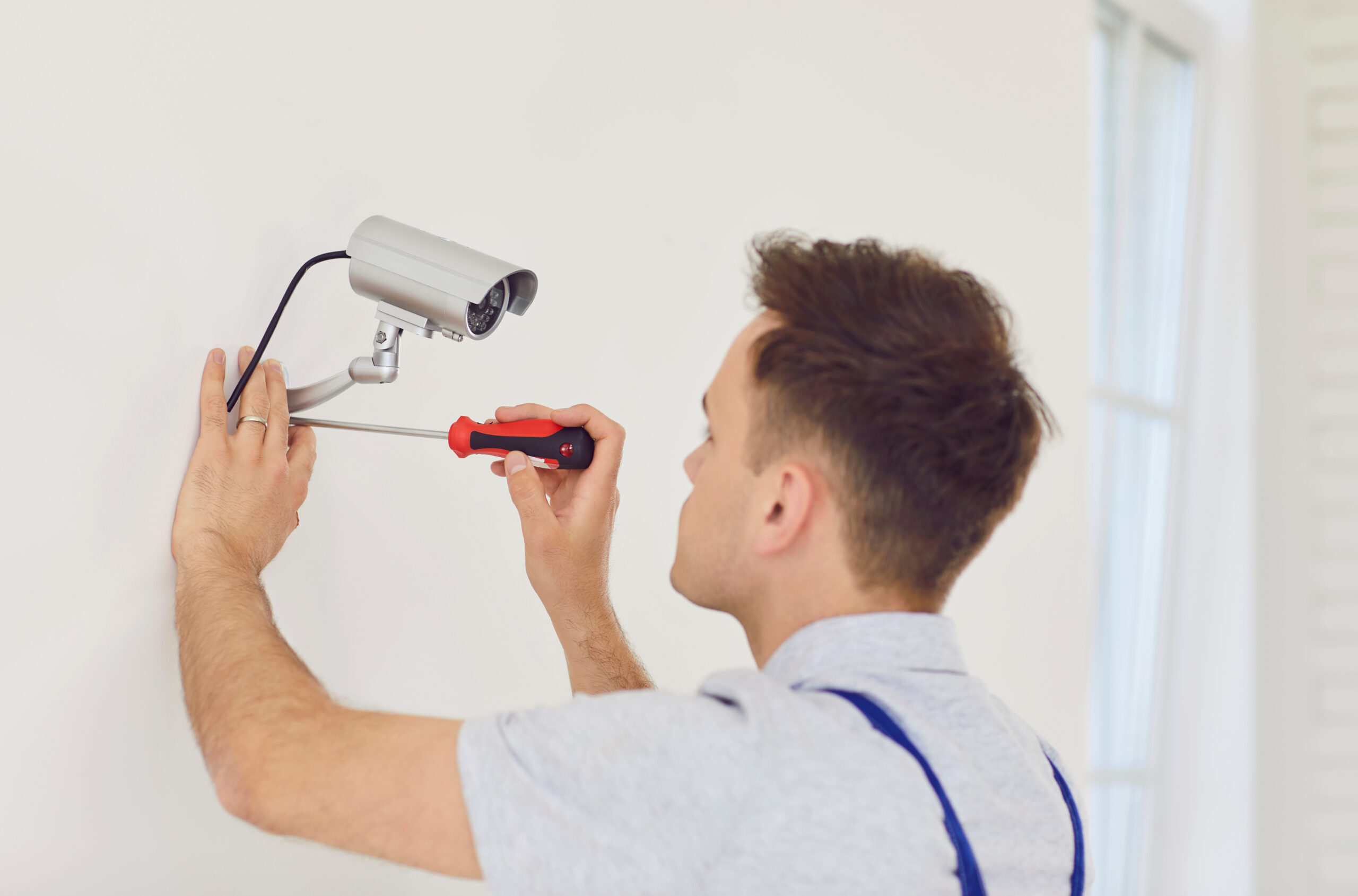 Young technician man in uniform installing surveillance CCTV camera on the wall indoors